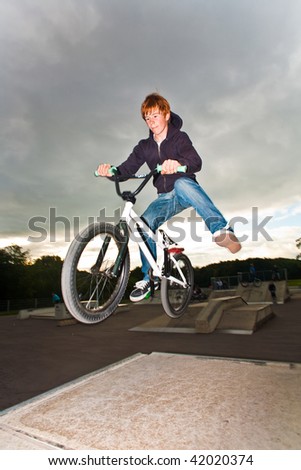 young red haired boy is jumping with his BMX Bike at the skate park with fun