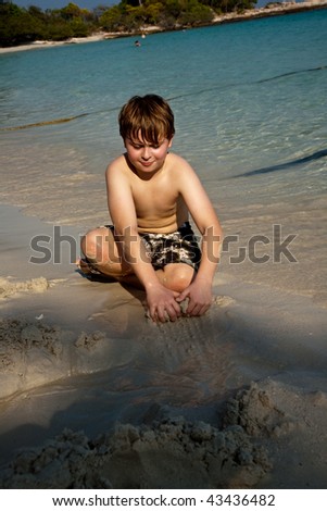 young boy is enjoying playing at the beach and building figures out of sand at the beautiful white beach