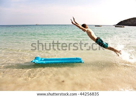 boy with red hair is enjoying jumping on the air mattress at the crystal clear water at a beautiful fine sandy beach