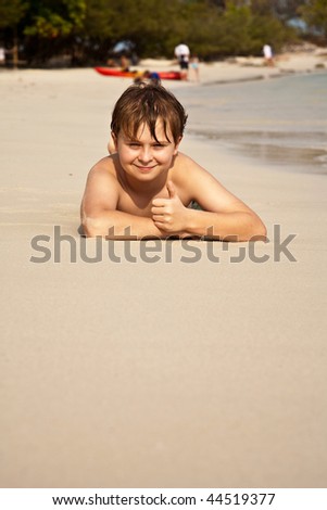 boy is lying at the beach and enjoying the warmness of the water and looking self confident and happy