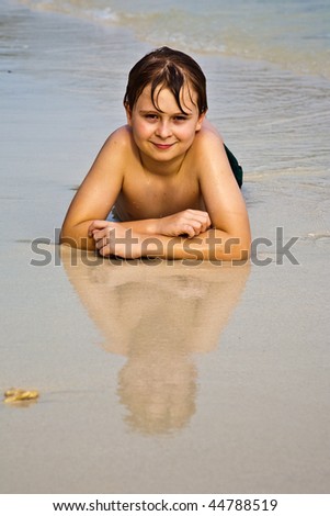 young boy is lying at the beach and enjoying the warmness of the water and looking self confident and happy