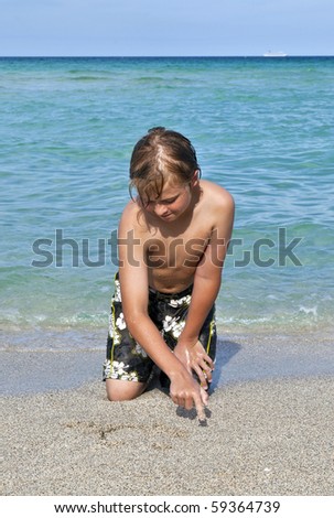 boy sits at the beach and plays with his hands in the water