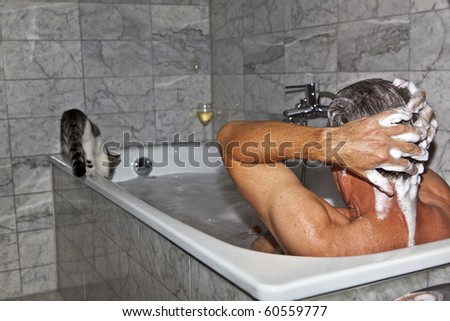 man bathing and cat strolling around the bath tube