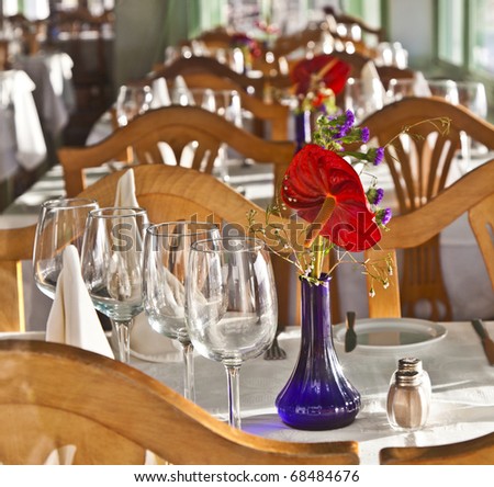 table is set in a restaurant with glasses, flowers and tablecloth