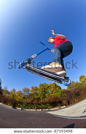 boy jumping with his scooter at the skate park under blue clear sky