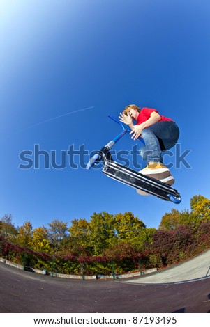 boy jumping with his scooter at the skate park under blue clear sky