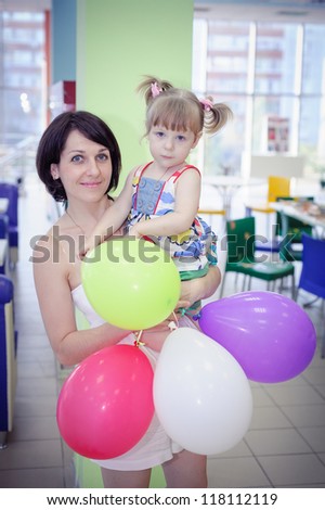 mother and funny child girl with bunch of colourful balloons in her hand.