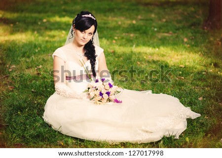 Attractive bride is sitting with bunch of flowers on the lawn. wedding dress. Bridal wedding bouquet of flowers