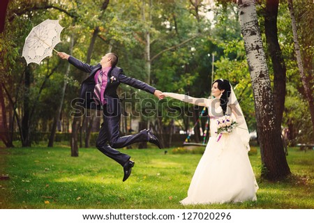 The groom departs on an umbrella  in a park. The bride holds the groom. groom flies on umbrella