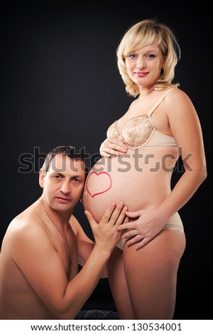 Portrait of a happy pregnant woman holding belly with heart drawn and of her husband. Happy family.