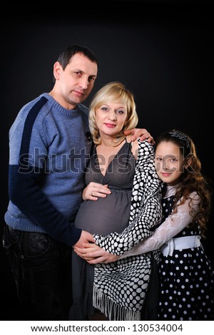 Portrait of a happy pregnant woman holding belly and of her husband and daughter. Happy family.