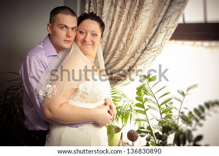 Bride and groom near the window. Bride and groom are standing against the window. portrait of newlywed couples of groom and bride in wedding suit. Married. Newlyweds stand beside window