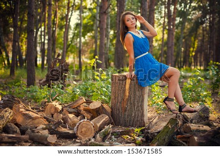 Teen girl in a blue dress in the forest on a background of wood park. fashion portrait of beautiful young female model lady woman  in bright blue dress posing outdoors near bush.