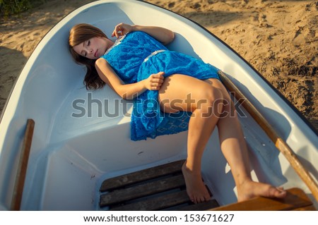 girl in blue dress lying in a boat. Beautiful woman striped dress posing in a boat at the sea.