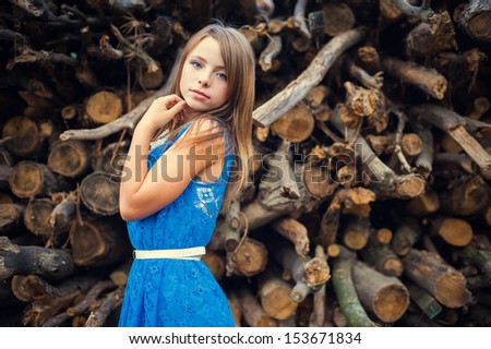 Teen girl in a blue dress in the forest on a background of wood. fashion portrait of beautiful young female model lady woman in blue dress posing outdoors near bush.