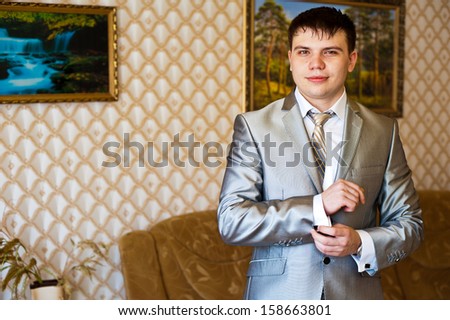Handsome groom thinking and putting on his bowtie while getting dressed for his wedding. Hands of wedding groom getting ready in suit.  man in a tux fixing his cuff link.