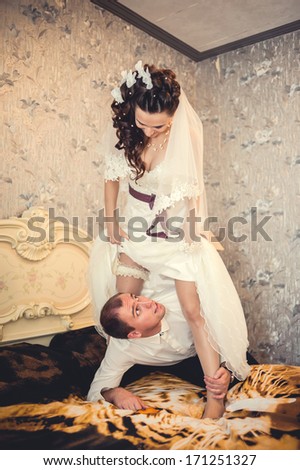 Funny bride sits on the neck of the groom. Wedding shot of bride and groom lying in a stylish bed