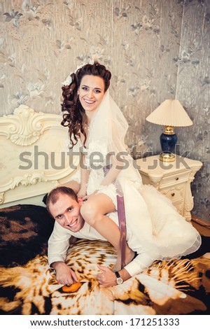 Funny bride sits on the neck of the groom. Wedding shot of bride and groom lying in a stylish bed