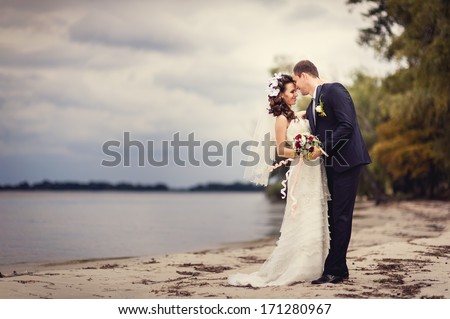 A wedding by the sea. Honeymoon. The bride and groom hugging on the shore of Lake. groom and bride hugging on a green lake. Groom and Bride in a park. wedding dress. Bridal wedding bouquet of flowers