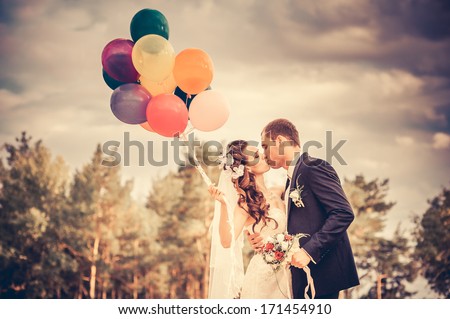 Beautiful Bride Holding Bunch Of Red Balloons On Park. Couple Of Bride And Groom With Balloons. Newlyweds With Balloons Outdoors. Happy Valentines Day!