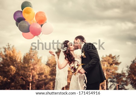 Beautiful bride holding bunch of red balloons on park. Couple of bride and groom with balloons. Newlyweds with balloons outdoors. Happy Valentines day!