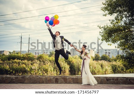 Groom flies on the balloons, but the bride holds his hand. Funny wedding. Groom jumps and flies on balloons. Young husband flying from his wife. Funny wedding concept. Happy Valentines day!