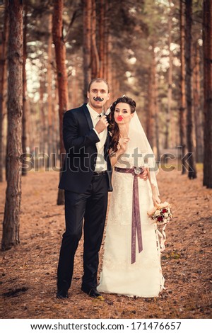 Wedding on the nature. couple in love bride and groom with a bouquet at bridal day in summer. Enjoy a moment of happiness and love and having fun with funny false mustache. playful newlywed family