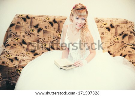 Gorgeous bride blonde in wedding dress in luxury interior posing at home and read the book. Romantic rich happy girl in bridal dress smiling have final preparation for wedding