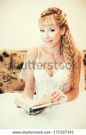 Gorgeous bride blonde in wedding dress in luxury interior posing at home and read the book. Romantic rich happy girl in bridal dress smiling have final preparation for wedding
