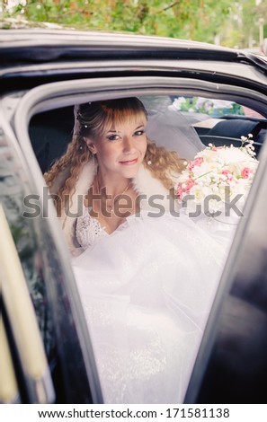 happy bride with flower bouquet siting in the car. Portrait of a pretty bride in a car