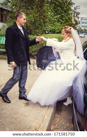 The bride comes out from the car with man\'s help. Happy bride and groom out of wedding limousine