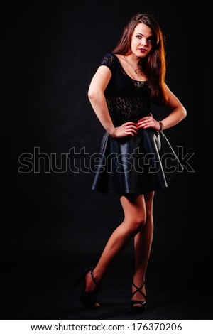 alluring sexy woman in evening dress posing over dark background. Young brunette lady in black dress posing on black background