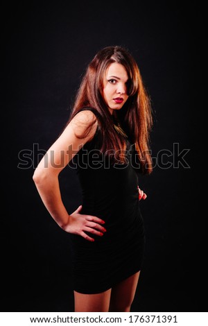 alluring sexy woman in evening dress posing over dark background. Young brunette lady in black dress posing on black background