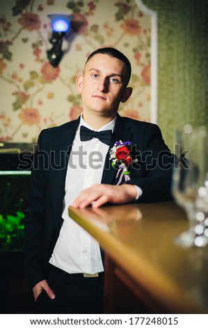 Handsome groom at wedding tuxedo smiling and waiting for bride  in a luxurious restaurant. Happy smiling groom newlywed. Rich groom at wedding day. Handsome caucasian man in tuxedo.