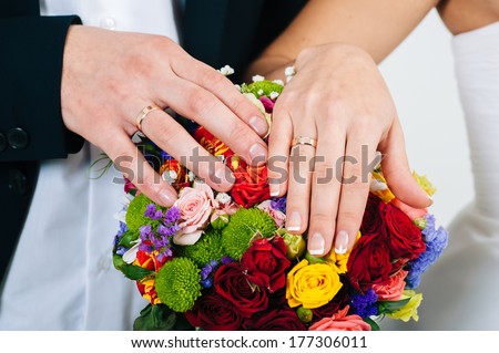 A newly wed couple place their hands on a wedding bouquet showing off their wedding bands. bridal bouquet and hands.