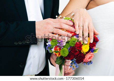 A newly wed couple place their hands on a wedding bouquet showing off their wedding bands. bridal bouquet and hands.