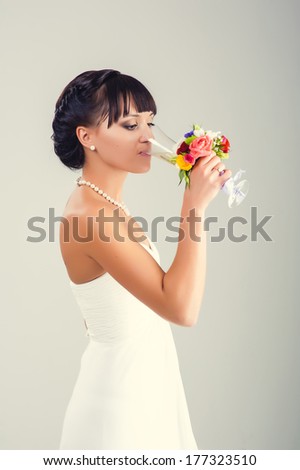 Wedding. Cheerful bride holding a champagne glass smiling at camera. glass of champagne in a hand of a bride.Bride drinking champagne. Happy holiday. Wedding bouquet of flowers and bridal dress