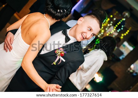 Wedding. Just married couple dancing in front of their unrecognizable friends. Kiss and dance young bride and groom in dark banqueting hall. Happy holiday of new family. Wedding bouquet, bridal dress