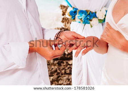 Newlyweds wear rings to each other on the background of the Caribbean. Groom put a ring on finger of his lovely wife. Wedding couple together. Closeup groom and bride hands in wedding ceremony