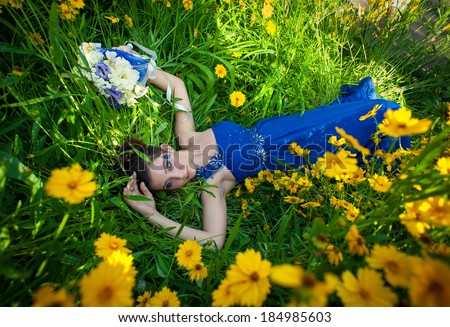 Beautiful young woman posing at field of flowers. bride in blue wedding dress in a grass. girl lying in a field of flowers