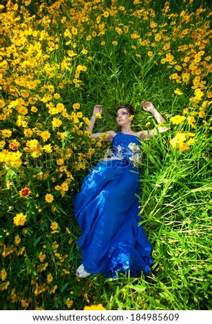 Beautiful young woman posing at field of flowers. bride in blue wedding dress in a grass. girl lying in a field of flowers