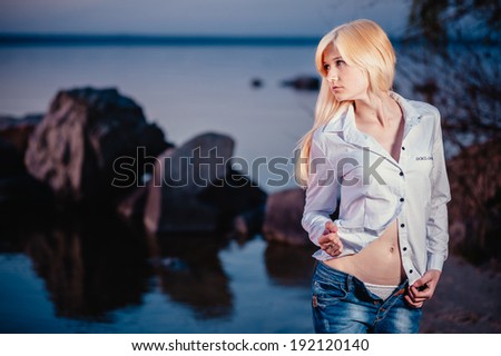 Blonde girl walking barefoot in jeans and a white shirt on the river at sunset. Walk on the water after work