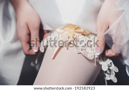 bride dresses garter on the leg. Picture of beautiful female barefoot legs in wedding dress. Bride dresses stockings on feet. Bride putting a wedding garter on her leg