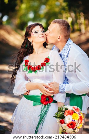 Ukraine. Happy ukrainian wedding (bridal) couple in the ukrainian style. Beautiful bride and groom in the ukrainian style are standing with bouquet. Female and male models.  park summer outdoor