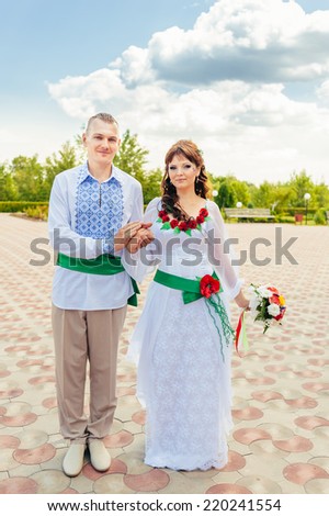 Ukraine. Happy ukrainian wedding (bridal) couple in the ukrainian style. Beautiful bride and groom in the ukrainian style are standing with bouquet. Female and male models. Indoors, close up.