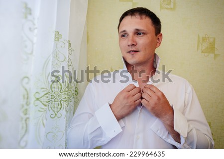 GROOM GETTING READY. A groom putting on cuff-links as he gets dressed in formal wear