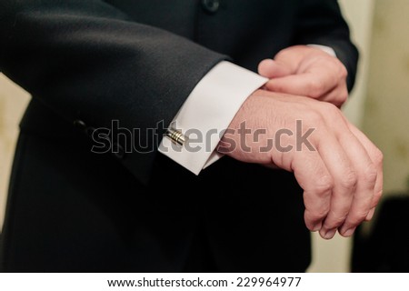 GROOM GETTING READY. A groom putting on cuff-links as he gets dressed in formal wear