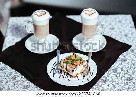 Cappuccino or latte coffee with heart shape. A cup of Coffee latte with heart design. Two cups of coffee on the table, latte art. cake on the plate