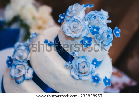 a multi level white wedding cake on a white base and blue flowers on top. Wedding cake in white and blue combination, adorned with flowers and ribbons