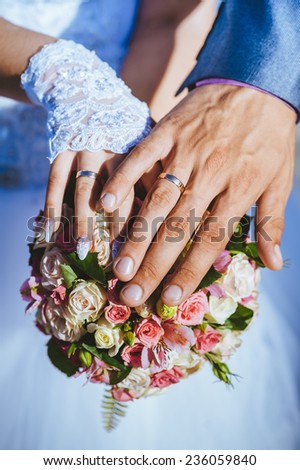 Hands of the groom and the bride with wedding rings and a wedding bouquet from roses